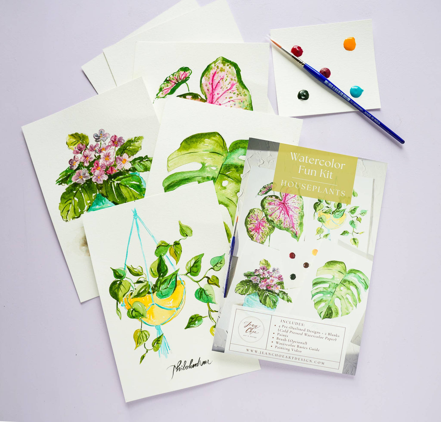 Finished watercolor plant paintings and a paintbrush on a light purple background