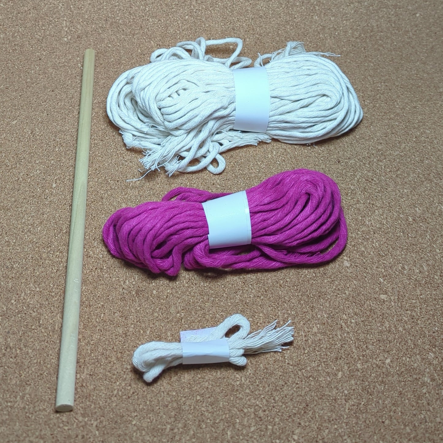 White and pink macrame cord with a wooden stick on a cork surface