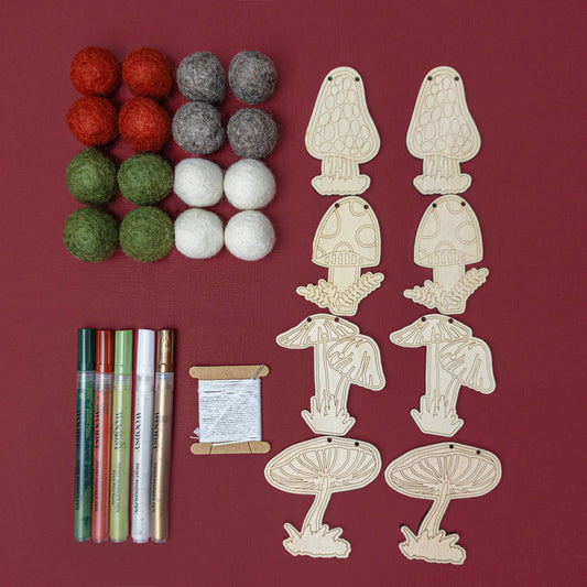 8 Mushroom-shaped wooden shapes, felt balls, paint markers, and thread with a needle on a red background