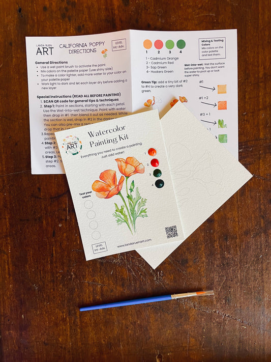 Watercolor painting kit with California poppy illustration on a wooden surface