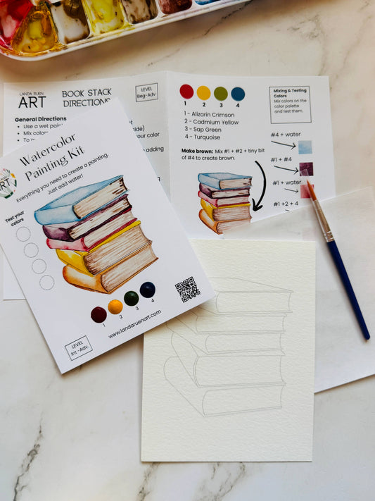 Watercolor painting kit, paint, and a paintbrush on a marble surface.