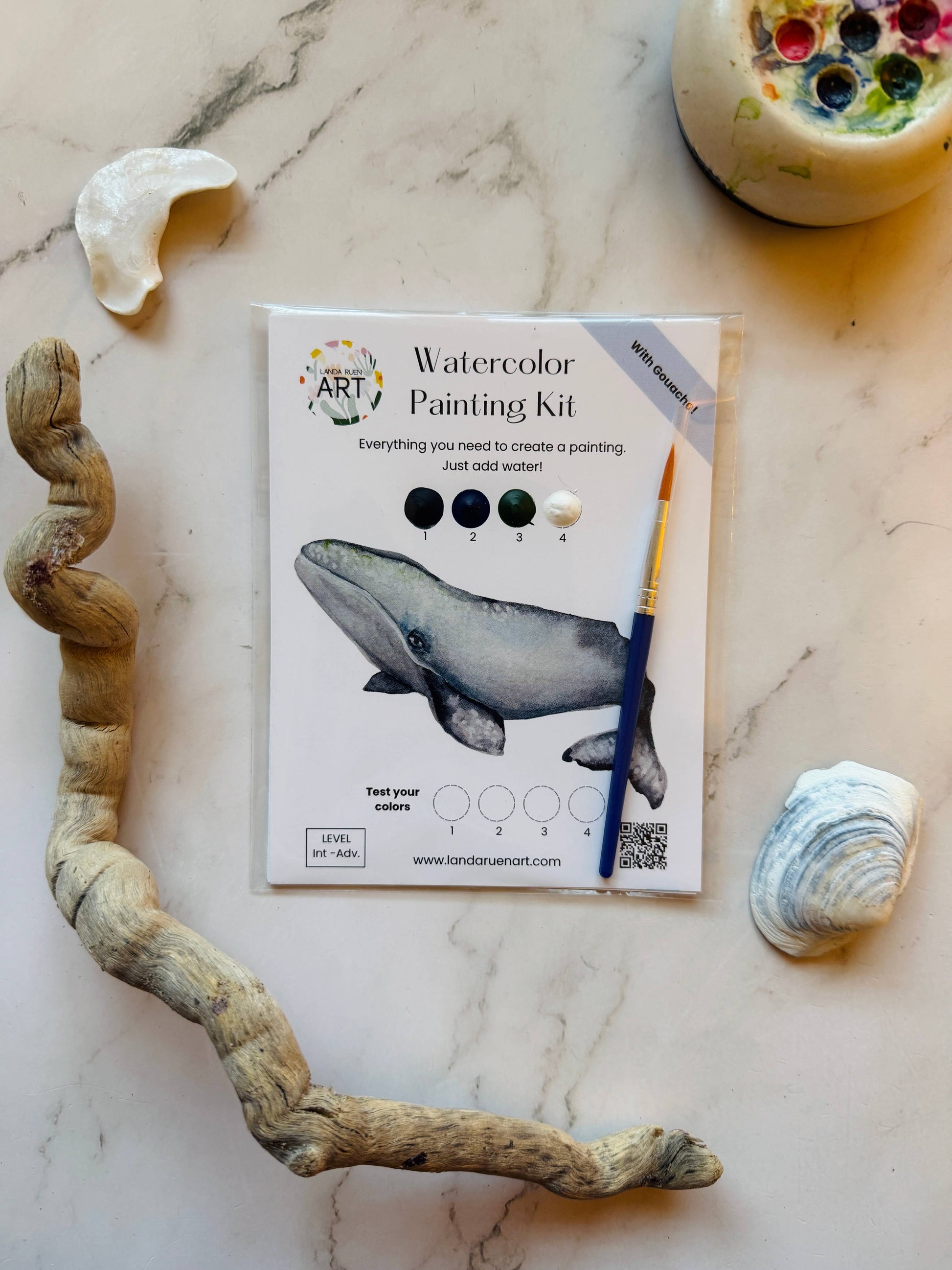 Watercolor painting kit with whale illustration on a marble surface with natural elements.