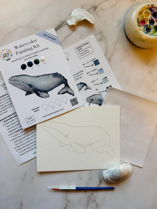 Watercolor painting kit with whale design, instructions, and paint supplies on a marble surface.