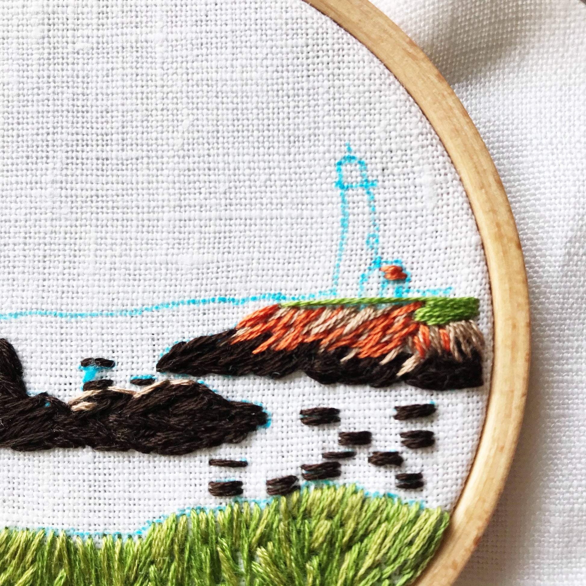Close up view of the embroidery hoop with a detailed landscape design on white fabric. The light blue ink from the soluble pen is visible.