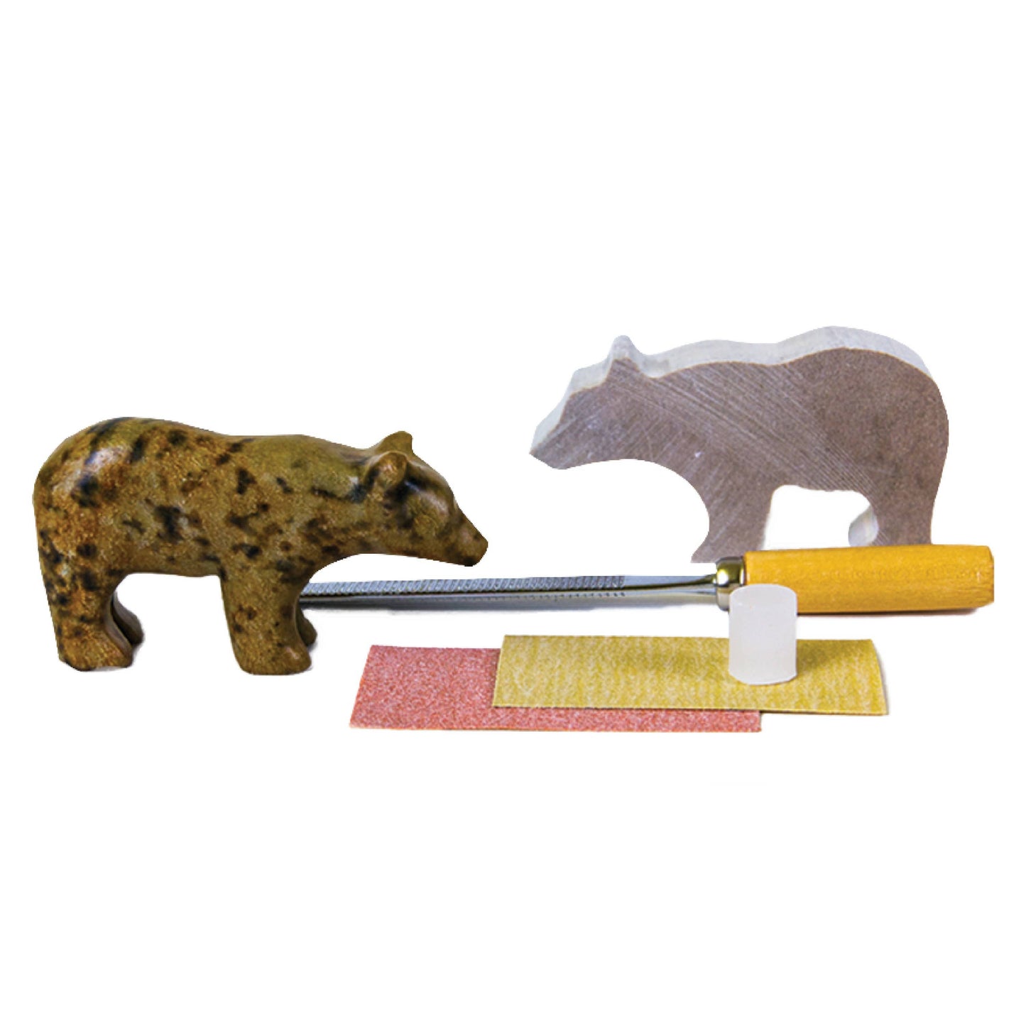 A finished soapstone bear carving next to the starting rough cut soapstone shape. Between them are the carving file, sandpaper, and nub of wax. 