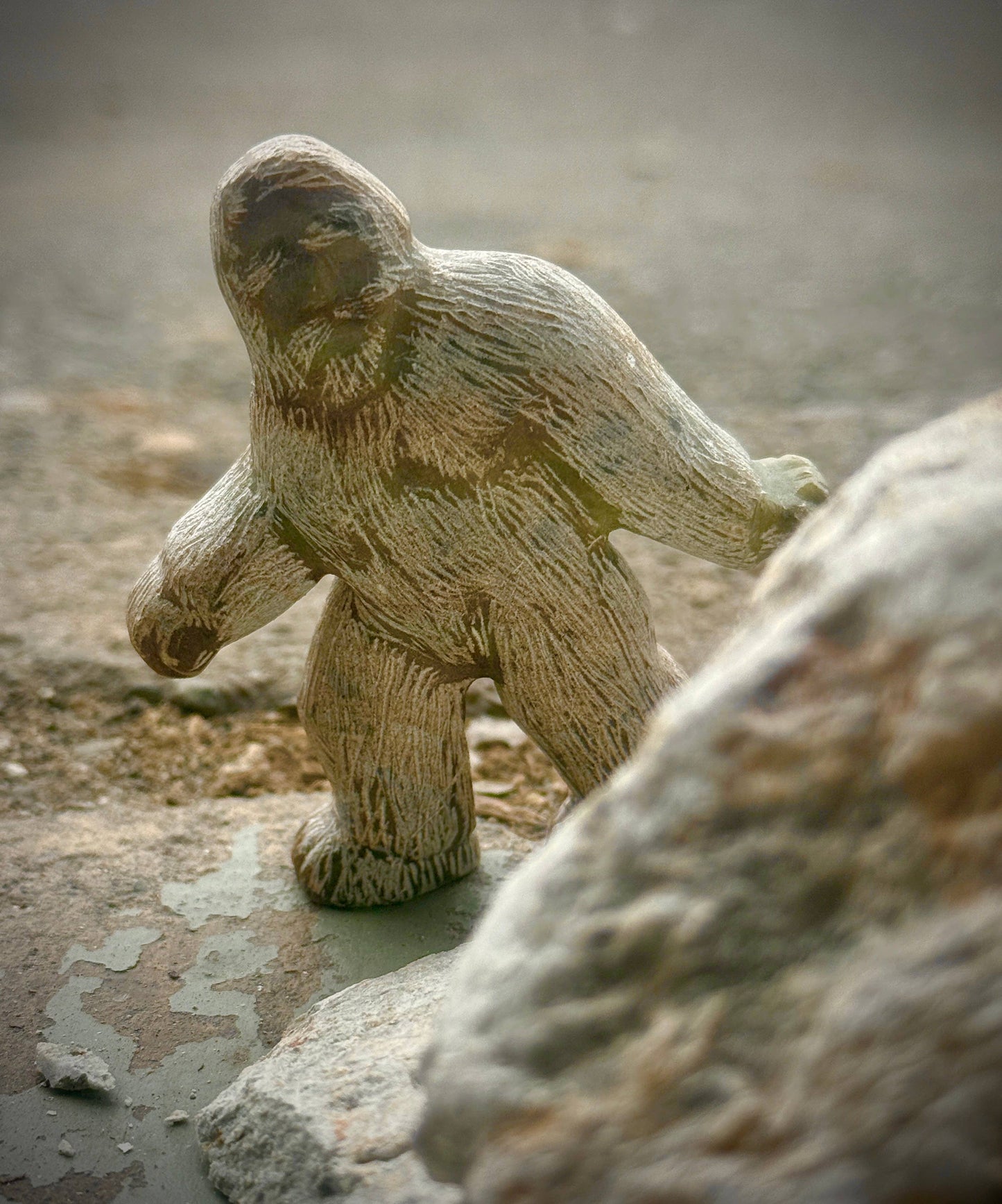 A finished Bigfoot soapstone carving surrounded by rocks.