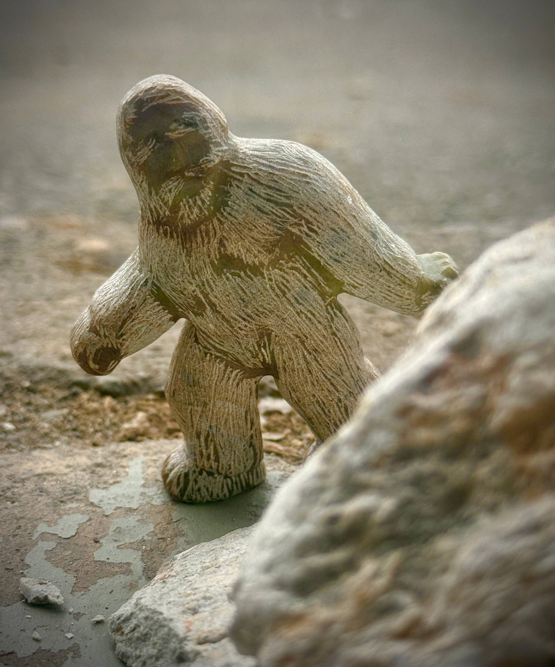 A finished Bigfoot soapstone carving surrounded by rocks.