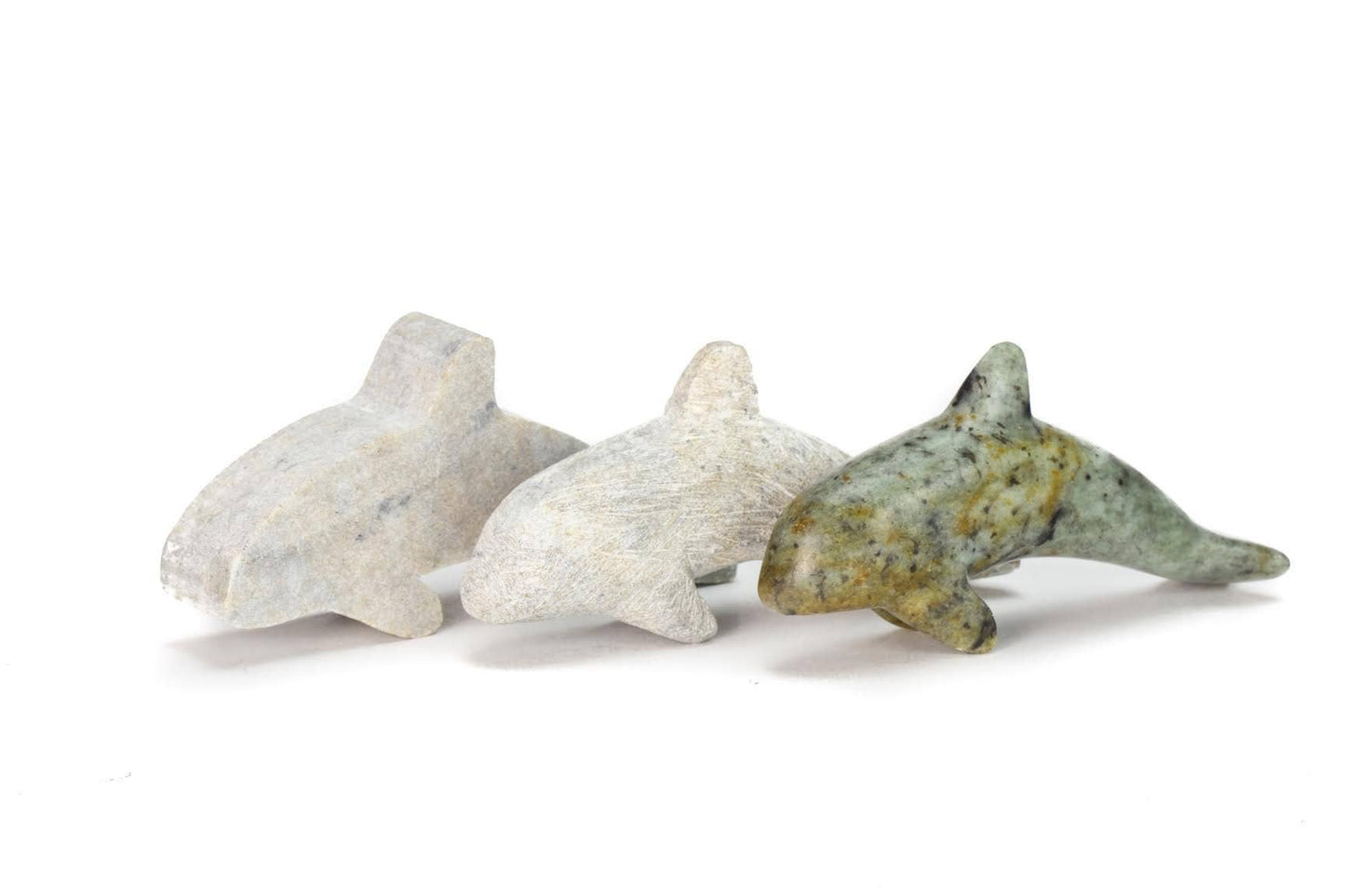 Three stone orcas on a white background beginning with the starting rough cut, a partially finished orca before being polished, and the finished orca with the design of the soapstone fully visible.