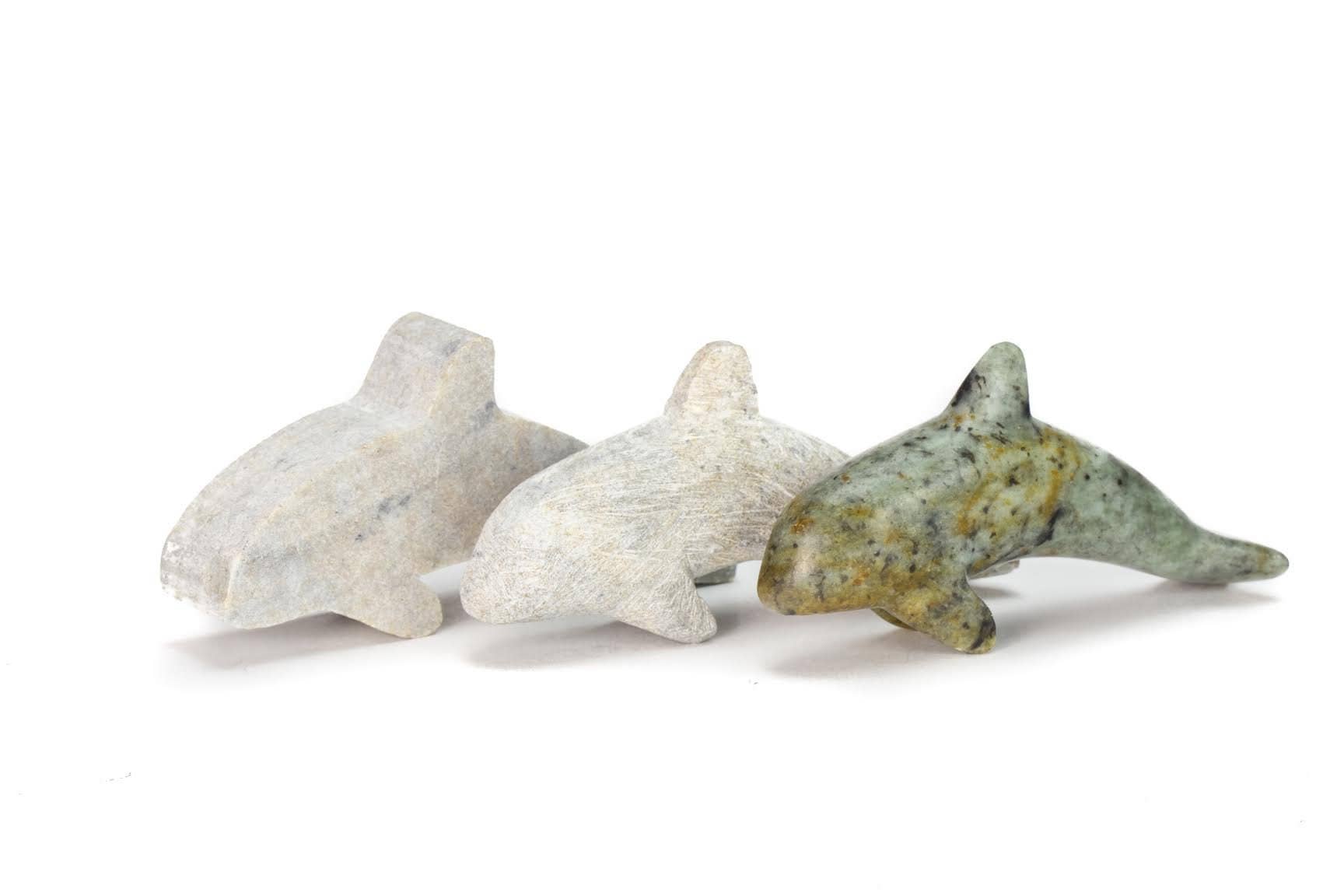Three stone orcas on a white background beginning with the starting rough cut, a partially finished orca before being polished, and the finished orca with the design of the soapstone fully visible.