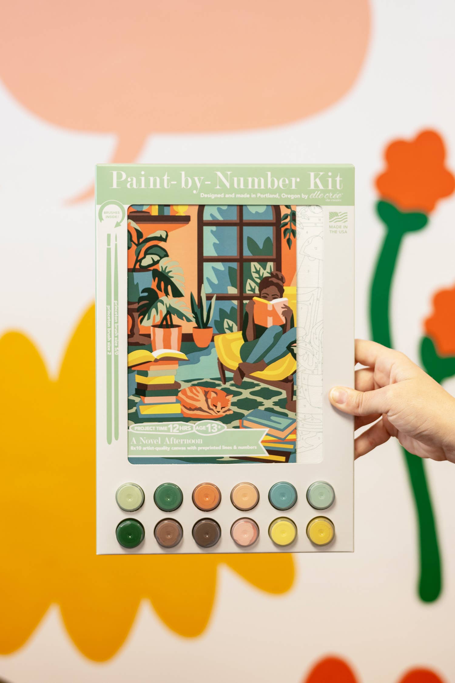 Paint-by-number kit held by a hand with colorful background