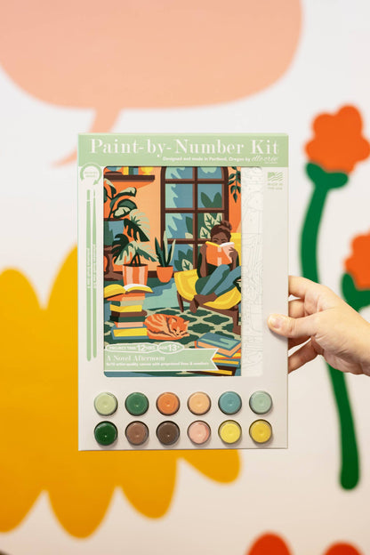 Paint-by-number kit held by a hand with colorful background