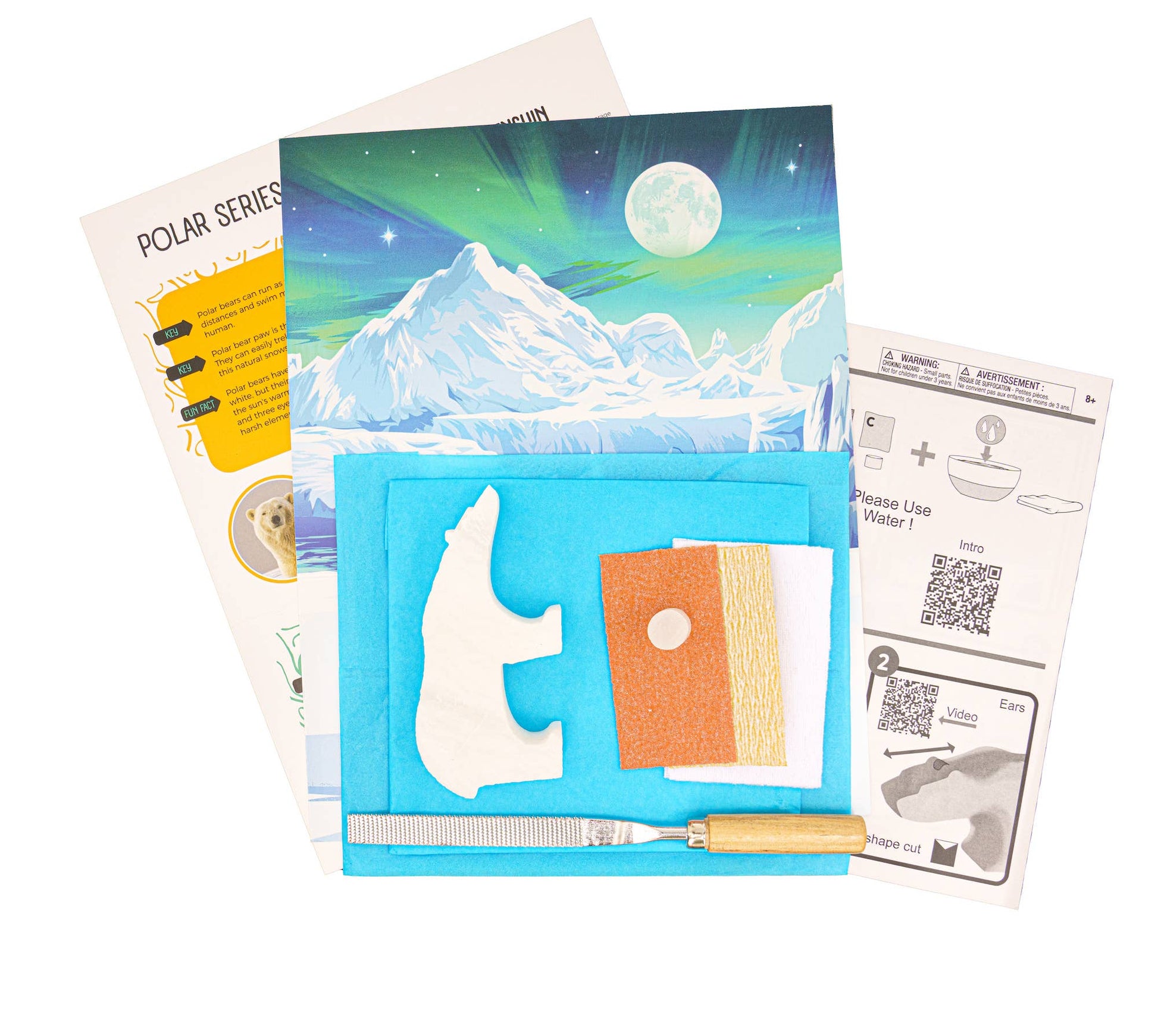 Carving kit with instructions, polar bear alabaster stone rough-cut blank, decorative diorama backdrop, and tools on a white background.