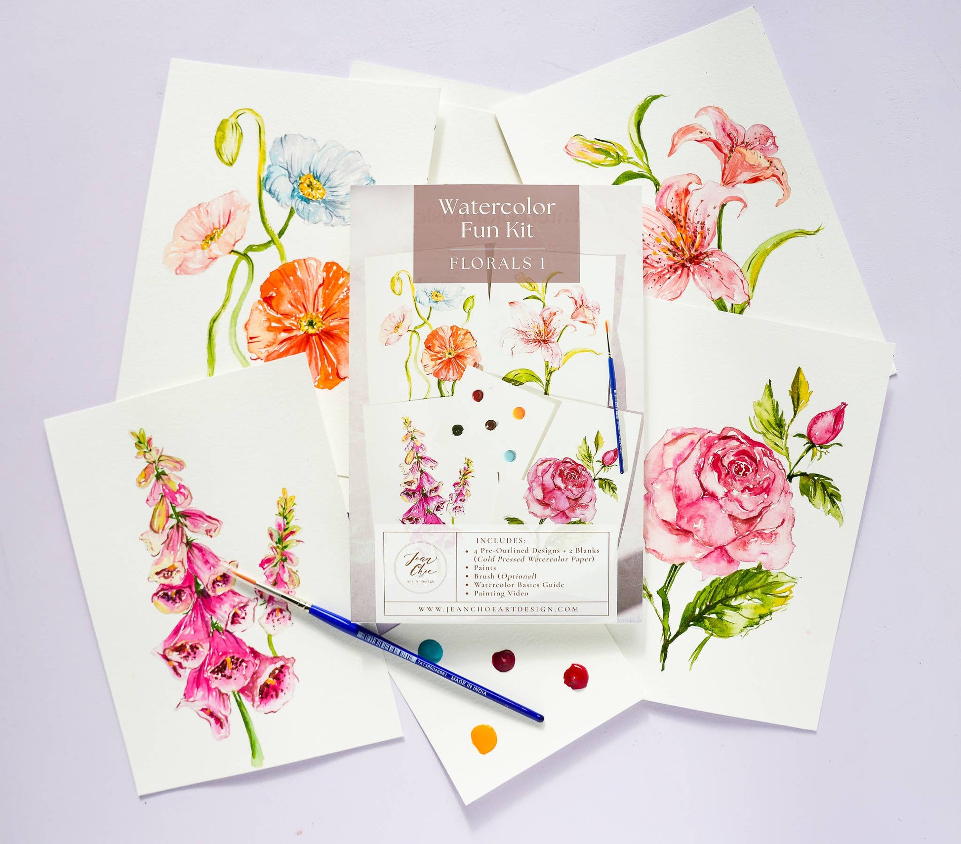Watercolor Kit with floral designs on paper and a paintbrush on a light purple background