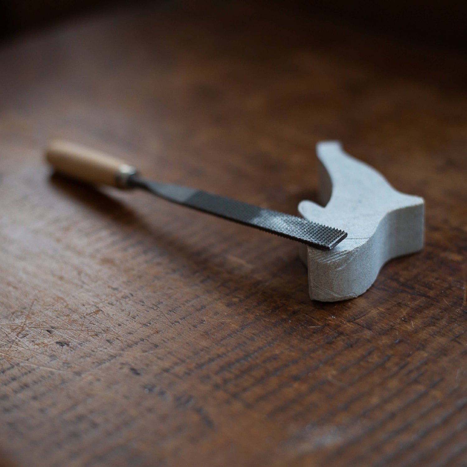 A close up view of a carving file and the original rough cut state of the orca, resting on a wooden surface.