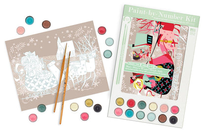 A Christmas-themed paint-by-number kit shown with its illustrated cover, a partially completed number sheet, two paintbrushes, and multiple round paint pans arranged on a white background.