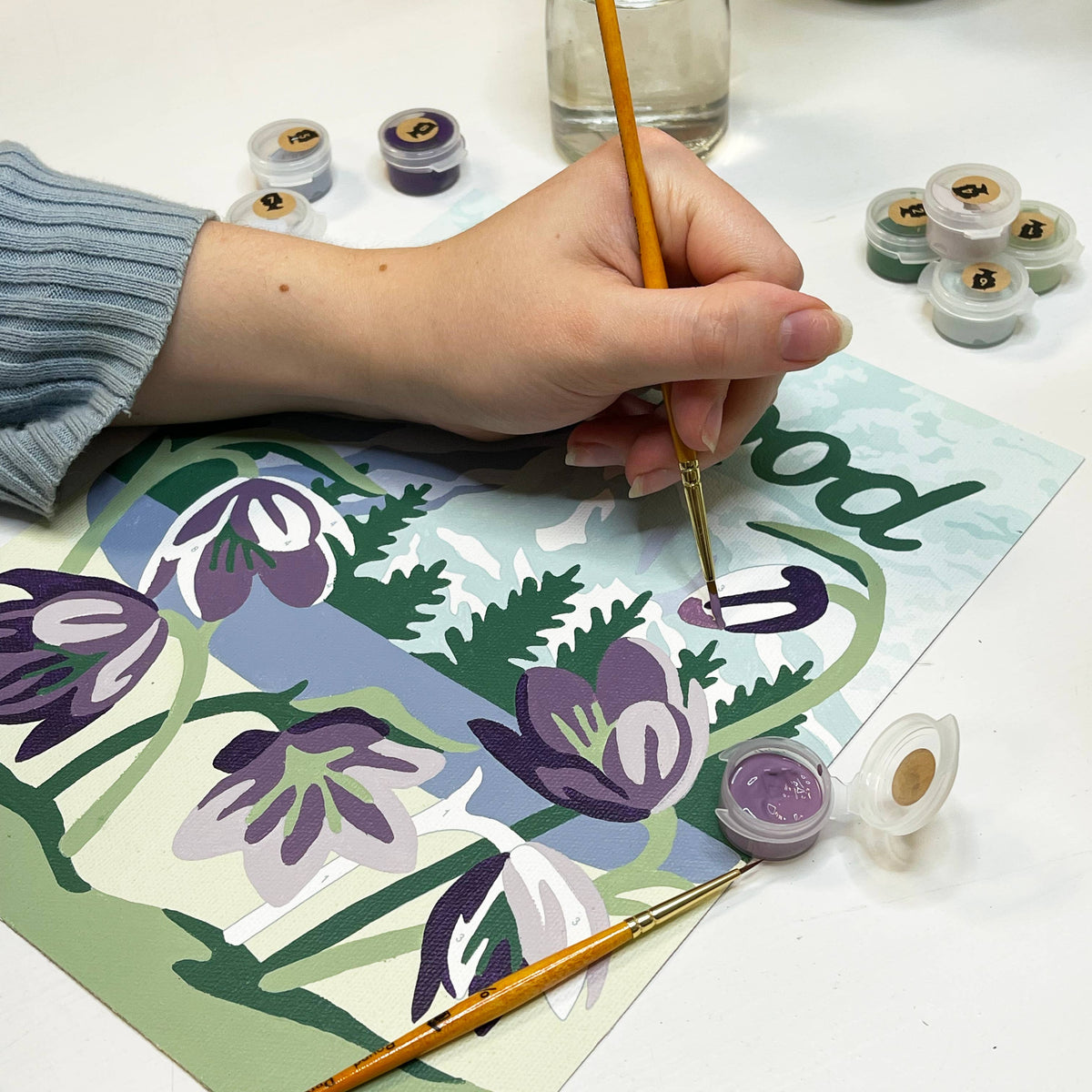Person painting a floral design with paint supplies around.