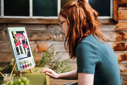 Woman looking at a painting of mushrooms on an easel outdoors.