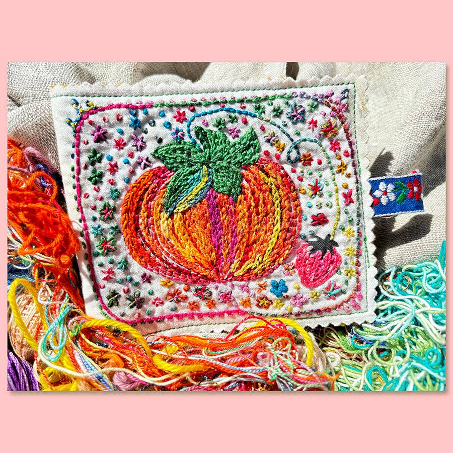 Embroidered patch of a tomato with colorful threads on a pink background