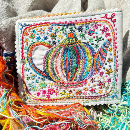 Colorful embroidered fabric with a teapot design on a textured beige background
