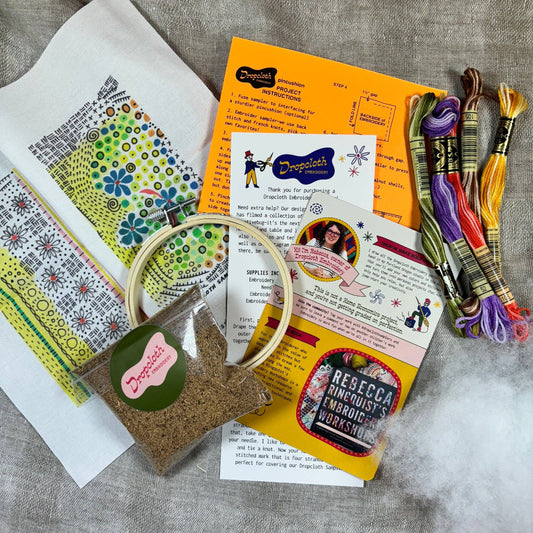 Embroidery kit with threads, patterns, sand, hoop, and instructions on a textured surface