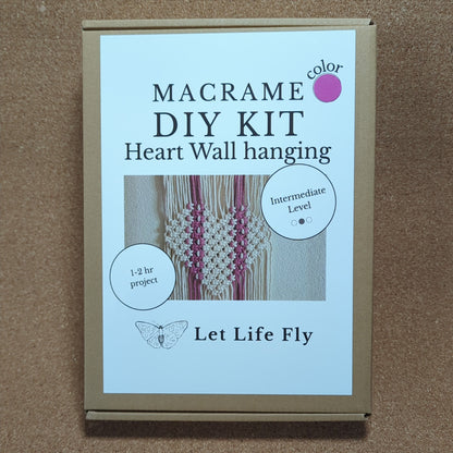Macrame DIY kit packaging with text and a small image of a heart wall hanging on a cork background