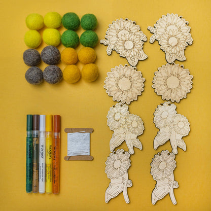 Felt balls, paint markers, thread with a needle, and wooden sunflower shapes