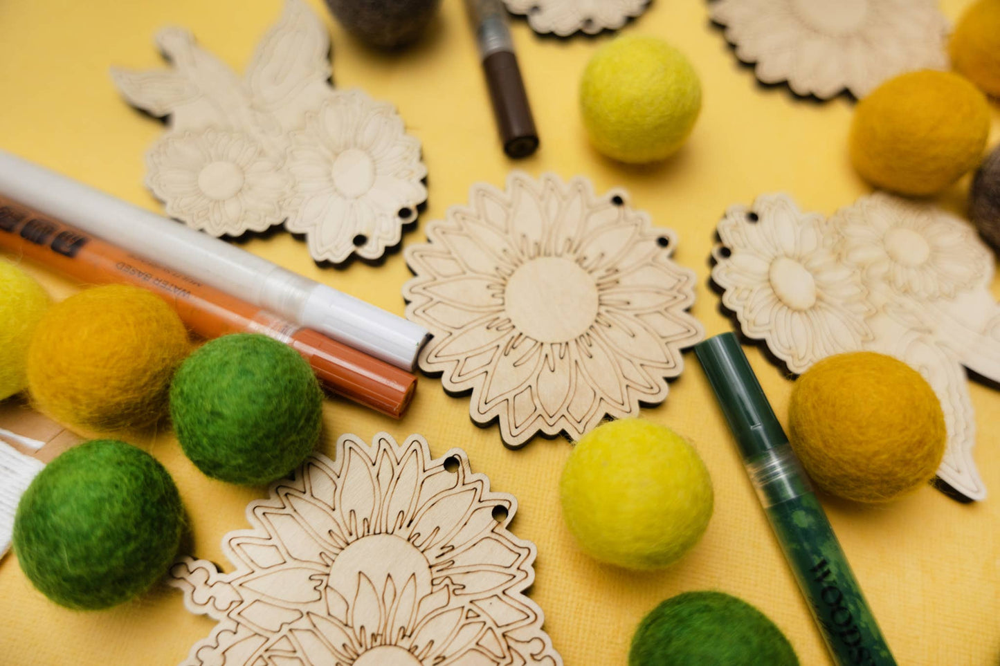 Paint markers with felt balls and unfinished  wooden sunflower shapes on a yellow background