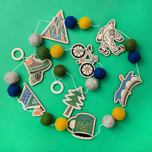 Decorative garland with nature adventures themed cutouts and colorful felt balls on a green background
