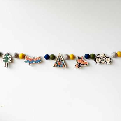 Decorative garland with nature adventure themed cutouts spaced with felt balls on a white background