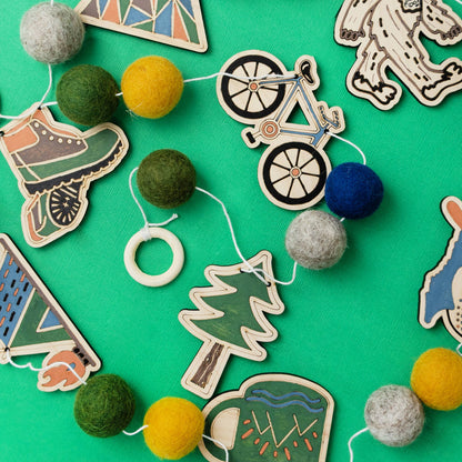 Decorative garland with colorful felt balls and wooden cutout shapes on a green background