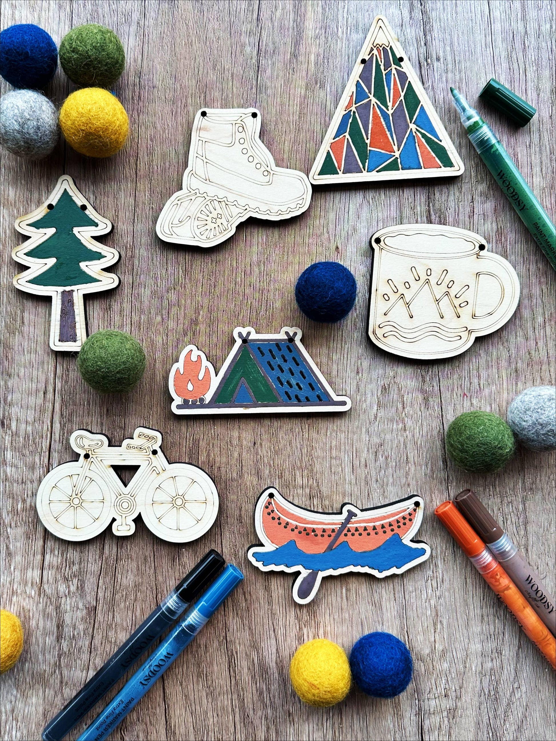 Nature adventure themed cutouts on a wooden surface with markers and felt balls. Some cutouts have been colored with the markers.