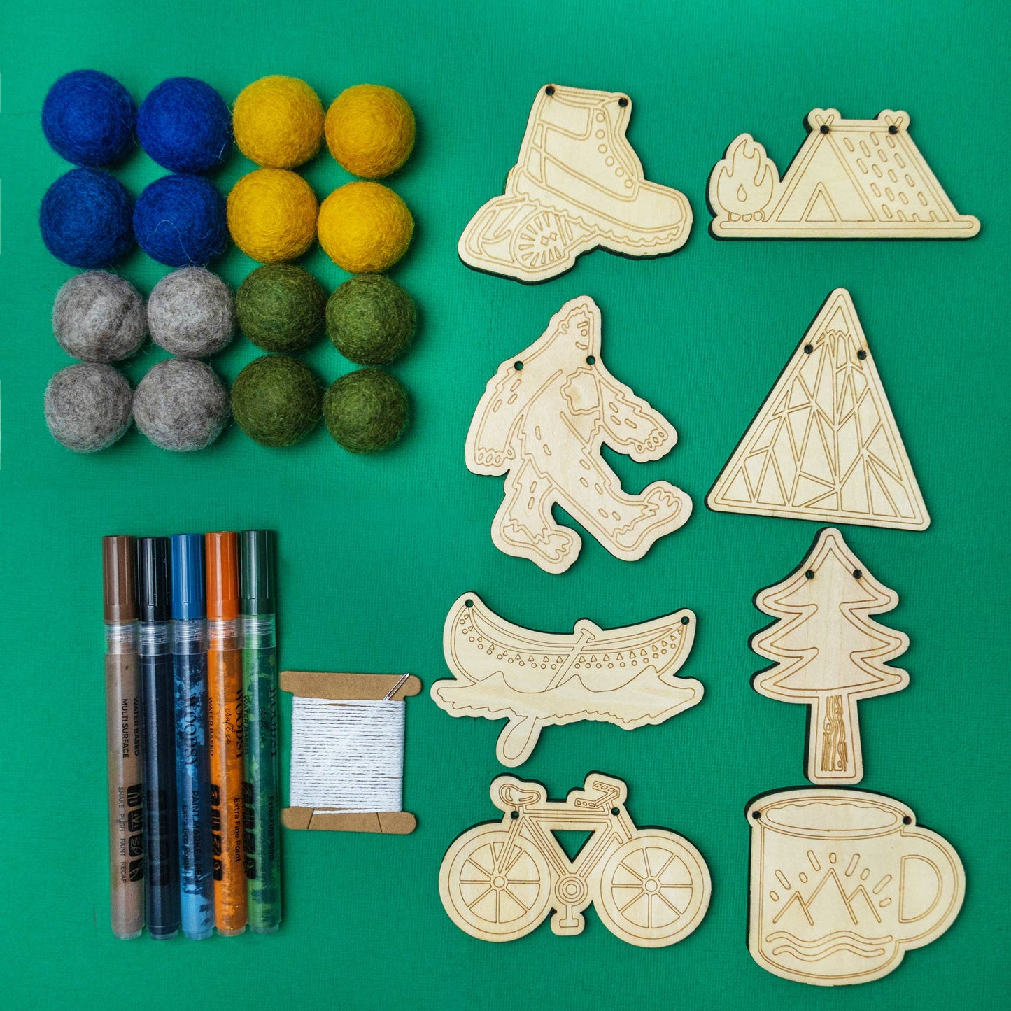 Garland supplies including felt balls, 2D wood cutouts, string, and paint markers on a green background.