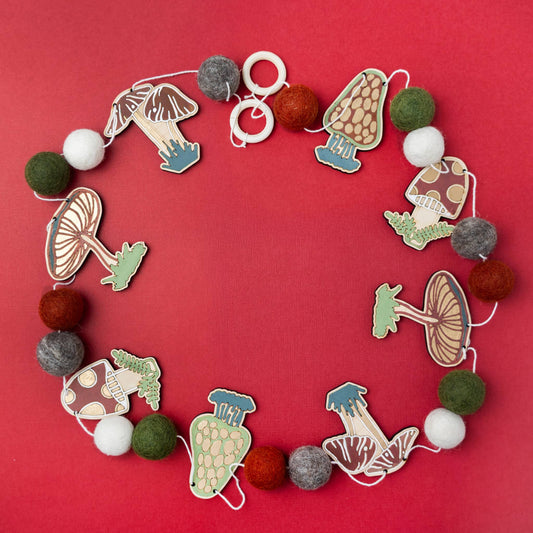 Garland of wooden mushroom shapes with felt balls on red background.