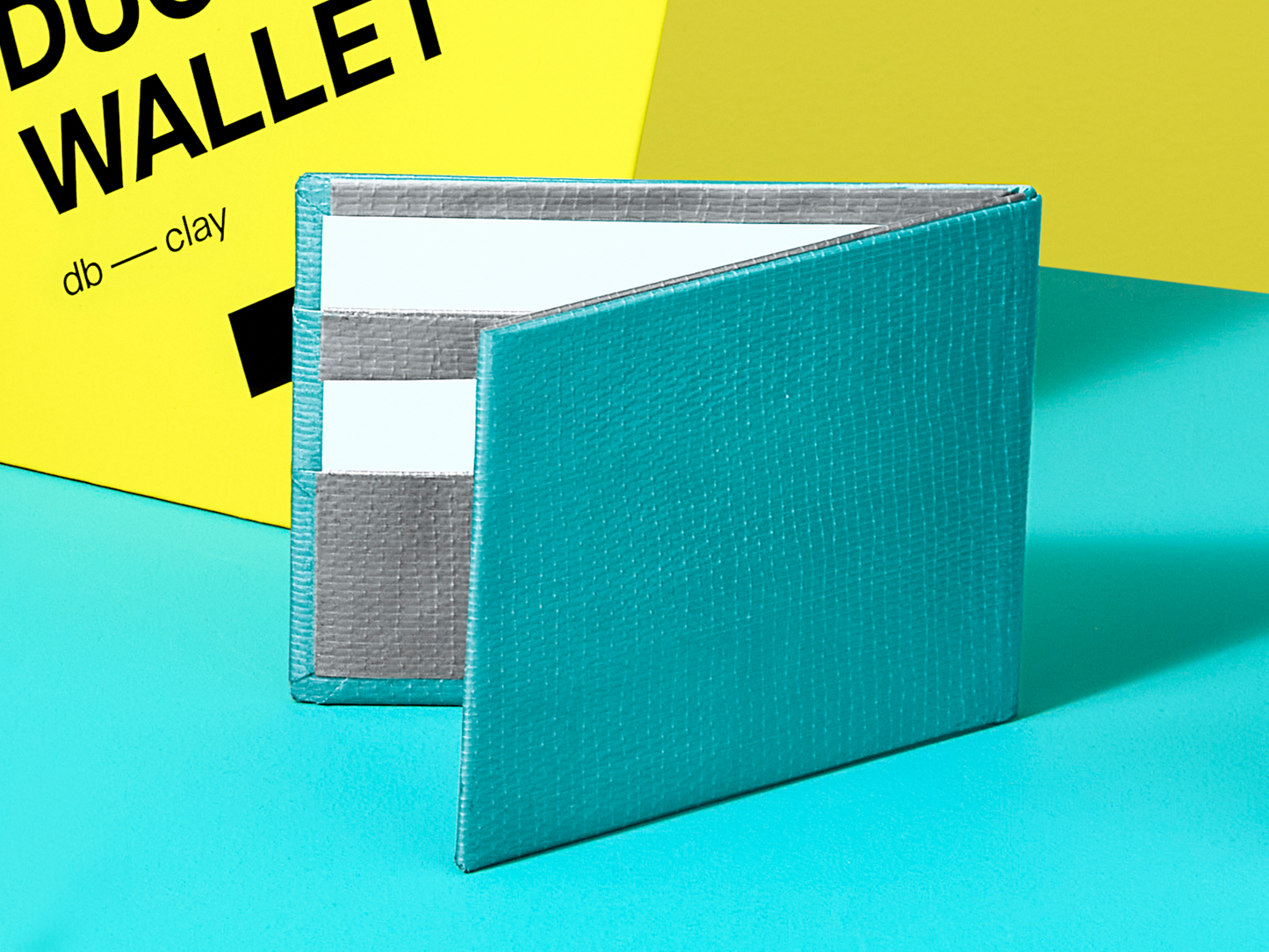 Teal wallet on a blue background with yellow and black packaging n the background