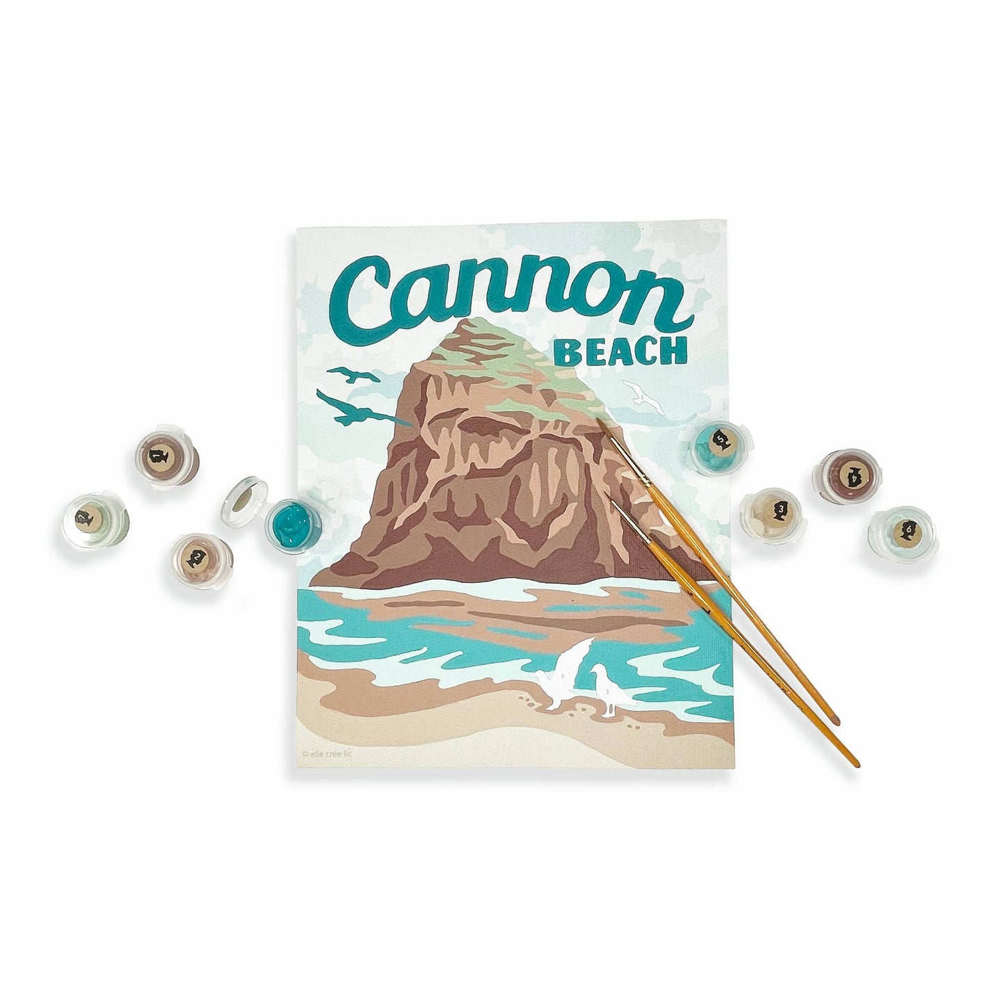 The completed paint-by-numbers painting of Cannon Beach with paintbrushes, and paints