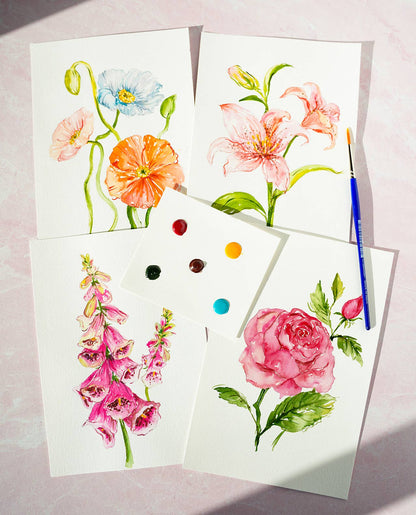 Finished watercolor flower paintings and a paintbrush on a light pink background