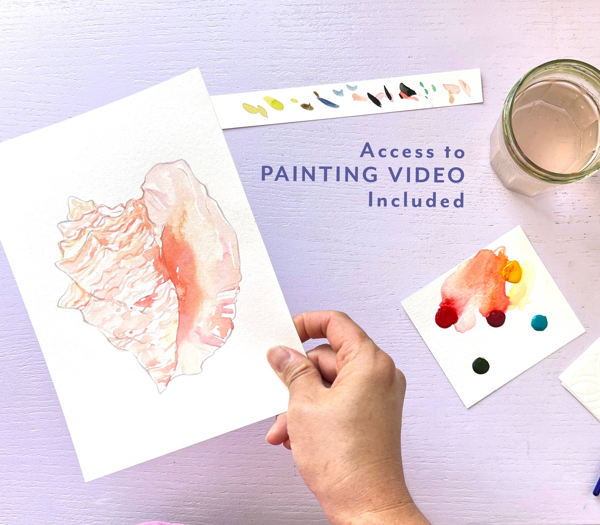 Hand holding a watercolor painting with additional samples and a jar on a light purple background.