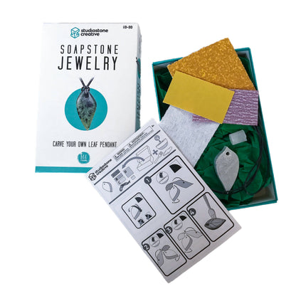 The product box next to the contents including the rough cut blank, sand paper, wax, instructions, waxed necklace. 