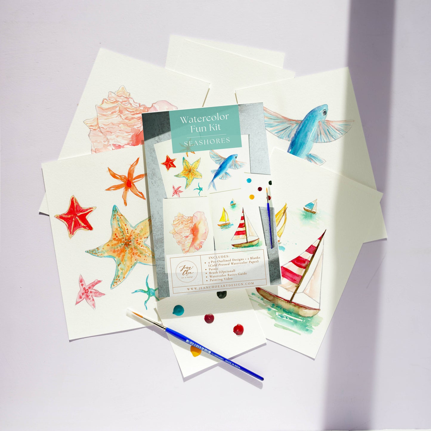 Watercolor art kit with watercolor paper, paintbrush, and watercolors on a light purple background