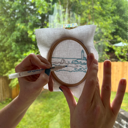Person holding an embroidery hoop  against a window tracing the design.