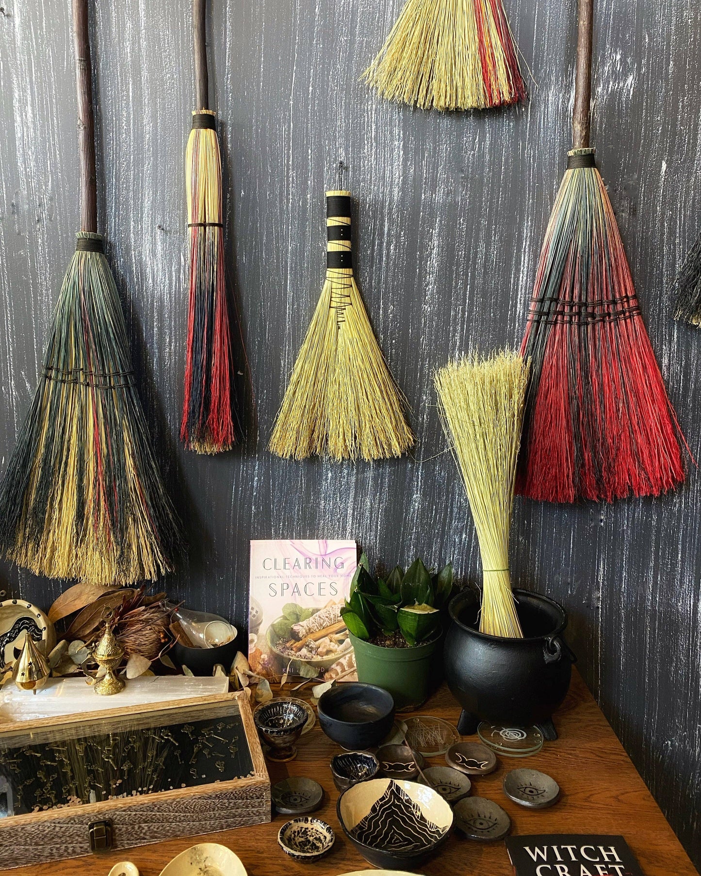 Decorative brooms hanging on a wall with various items on a table below.