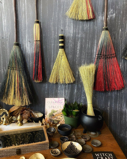 Decorative brooms hanging on a wall with various items on a table below.
