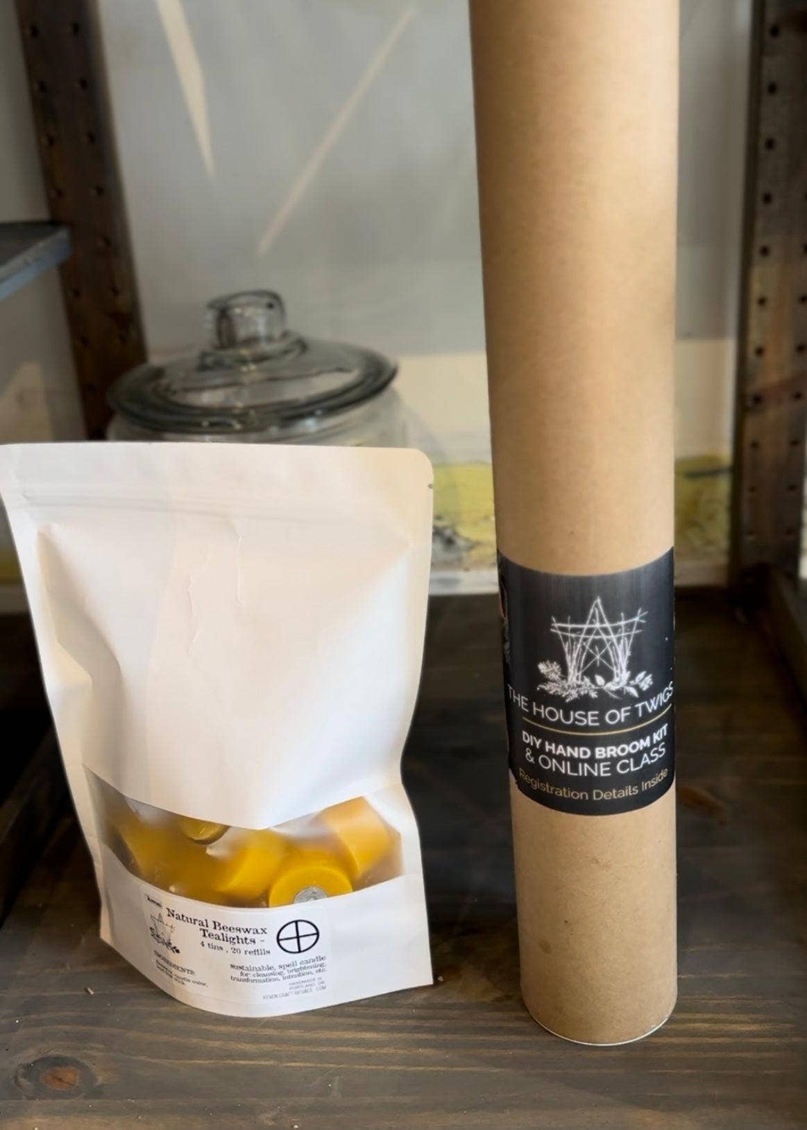 A tube containing the materials for the hand-broom, next to a bag of tealights for size comparison