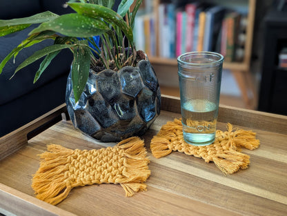 Glass of water on a wooden tray with decorative macrame coasters and a plant in the background.